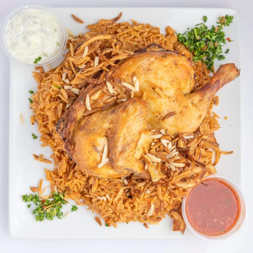 Middle-Eastern roasted chicken with rice, fried onions, almonds, and two dipping sauces.