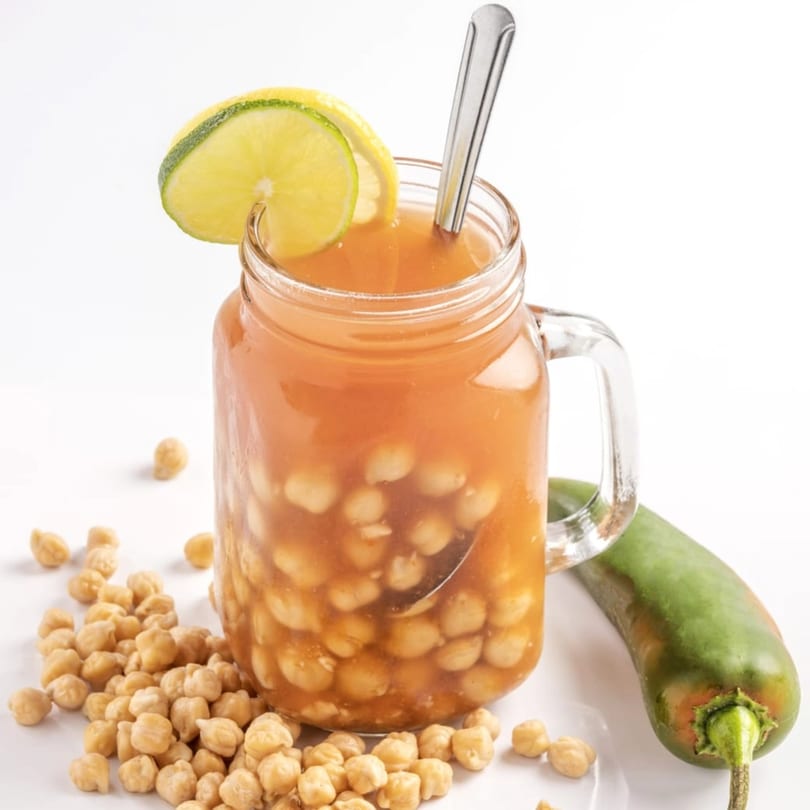 A glass mug of Kenz Cairo's chickpea soup, garnished with lime and a green pepper.