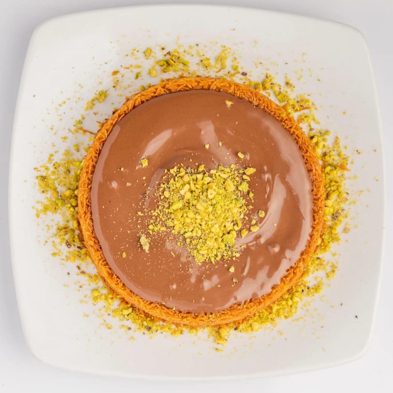 Kenz Cairo's kunafa with chocolate and crushed pistachios, presented on a white square plate.