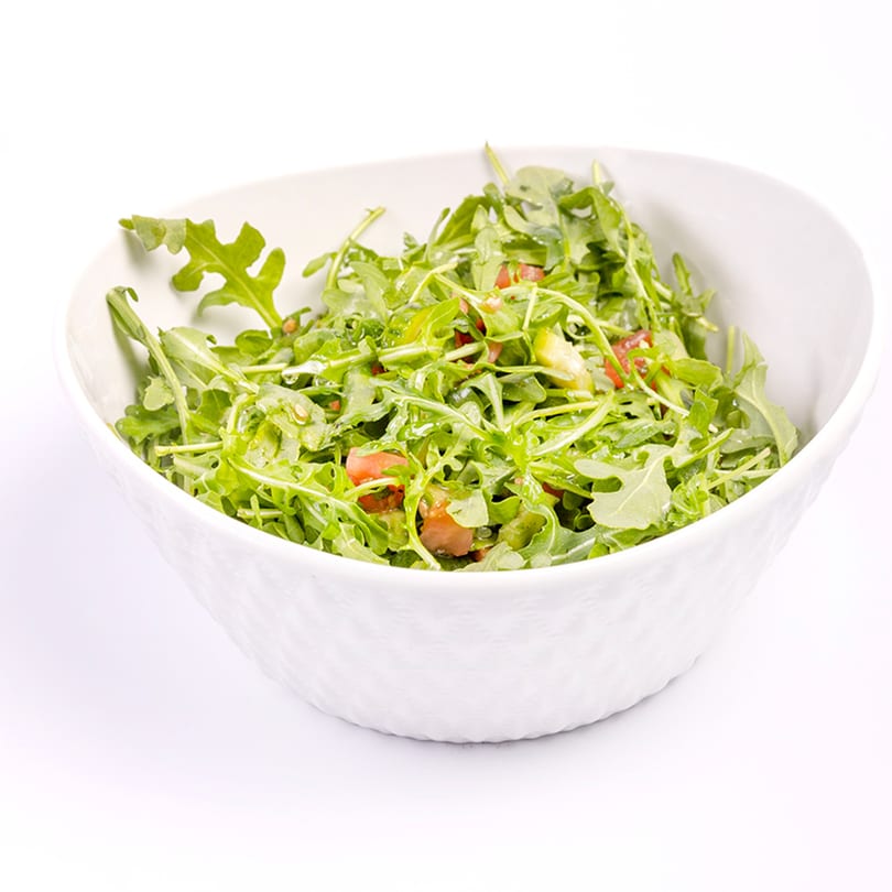 A white bowl filled with fresh green arugula salad, diced tomatoes, and a light dressing.